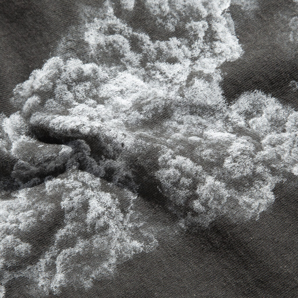 Dettaglio del tessuto di una t-shirt scura con una stampa chiara raffigurante una texture simile a una formazione naturale.