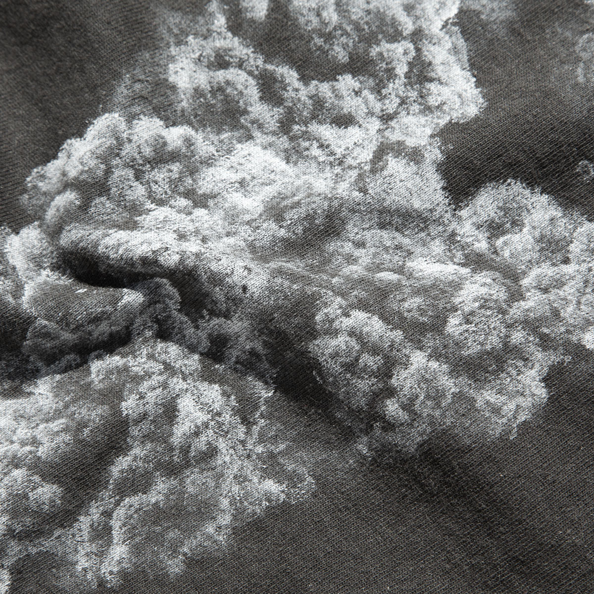 Dettaglio del tessuto di una t-shirt scura con una stampa chiara raffigurante una texture simile a una formazione naturale.
